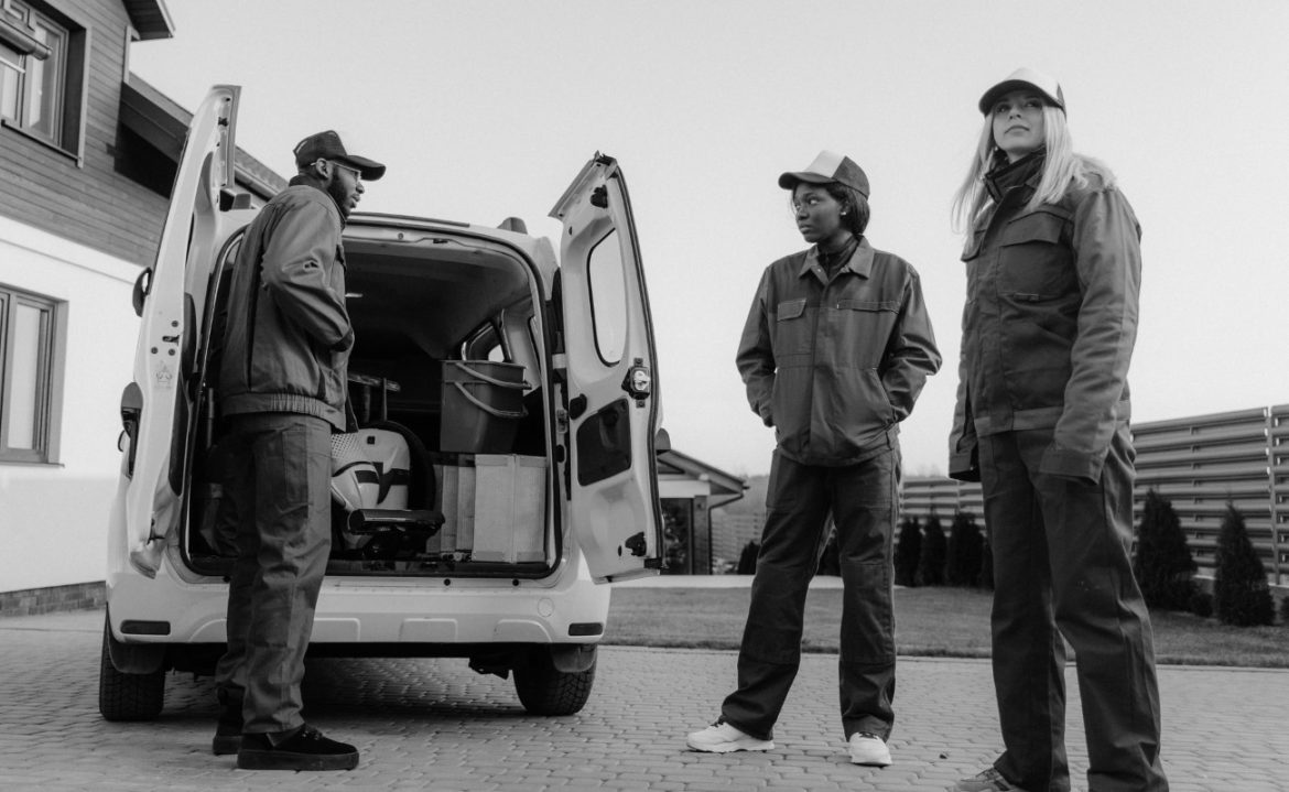 A black and white photo of three workers in overalls standing by a service van.