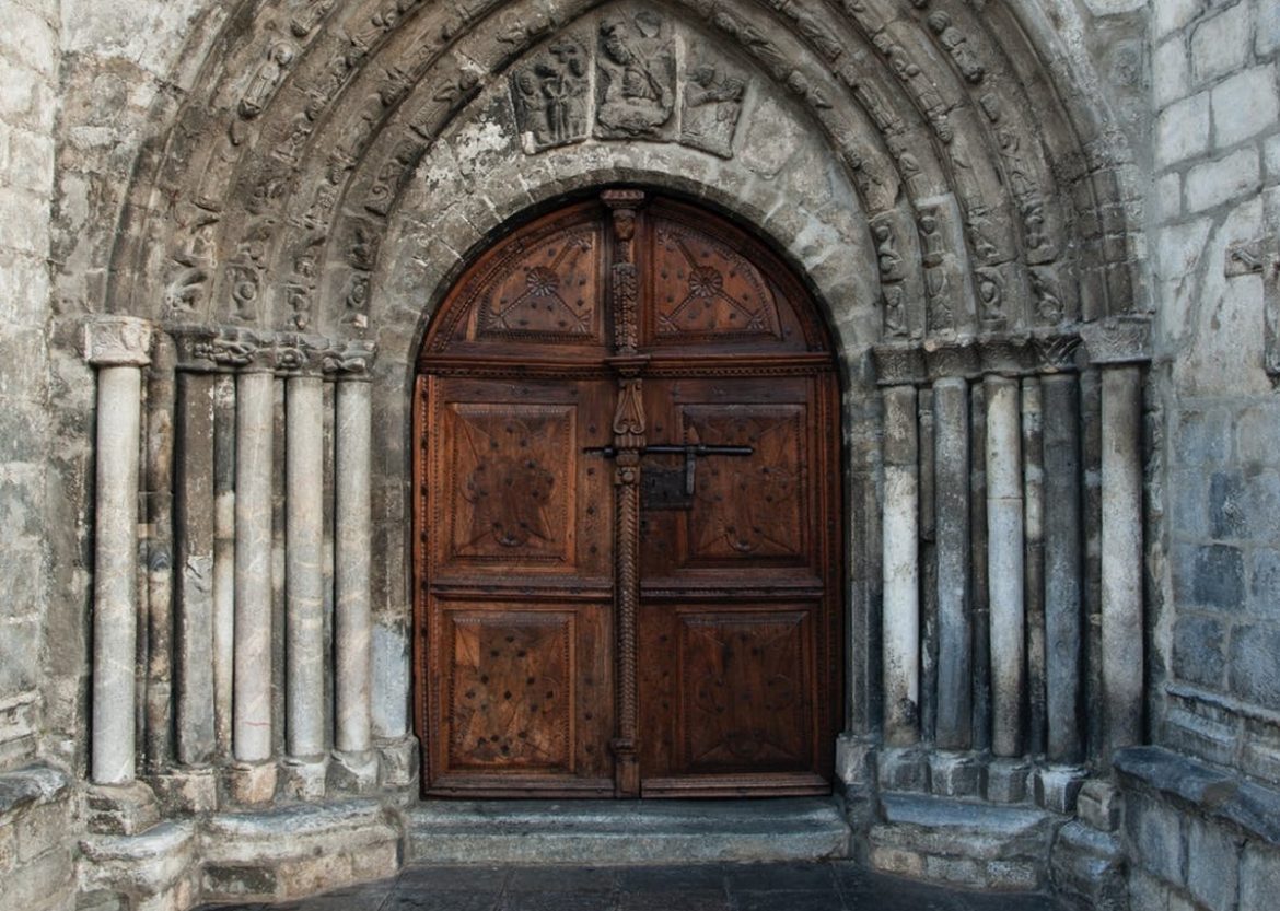 A photograph of the heavy wooden door of a monastery, framed in stone.