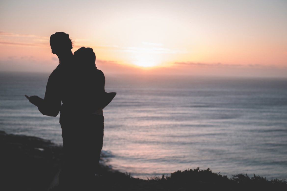 A photograph of a couple in silhouette, standing on the coast.