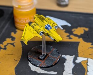 A picture of the model on the painting table. One wing remains primed and white, while much of the rest of the model is painted.